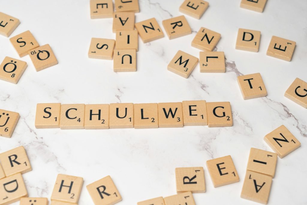 Scrabble tiles arranged to spell 'Schulweg' on a white marble surface, creative layout.