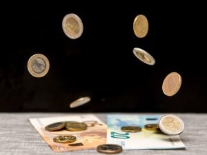 Dynamic image of euro coins and banknotes cascading onto a table against a black background.